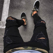 Black streetwear ripped jeans with distressed detailing paired with sneakers.