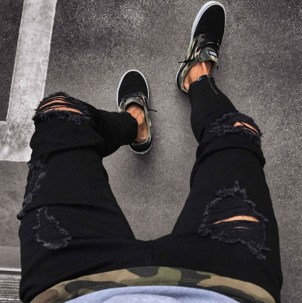 Black streetwear ripped jeans with distressed detailing paired with sneakers.